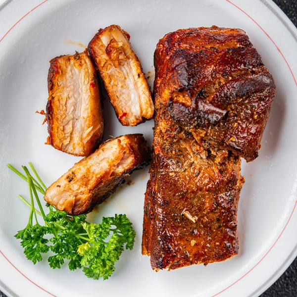 Close-up of succulent Chinese-style roasted pork belly slices with fresh parsley on a white plate.