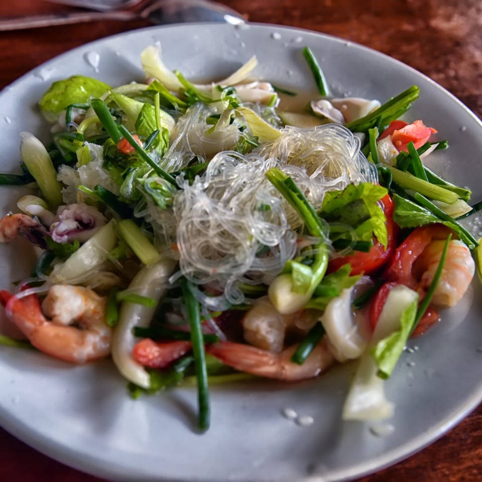 A vibrant Chinese seafood salad with clear noodles, shrimp, squid, and fresh green vegetables.
