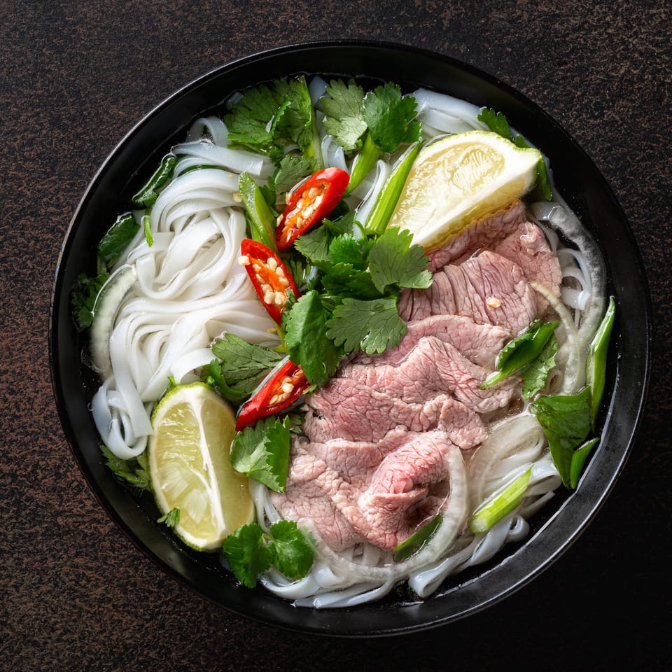 A bowl of pho with rice noodles, thinly sliced beef, cilantro, lime, and red chilies.