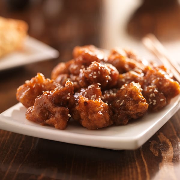 Close-up of sesame chicken from Yin Yang Express, glistening with sauce on a white plate.